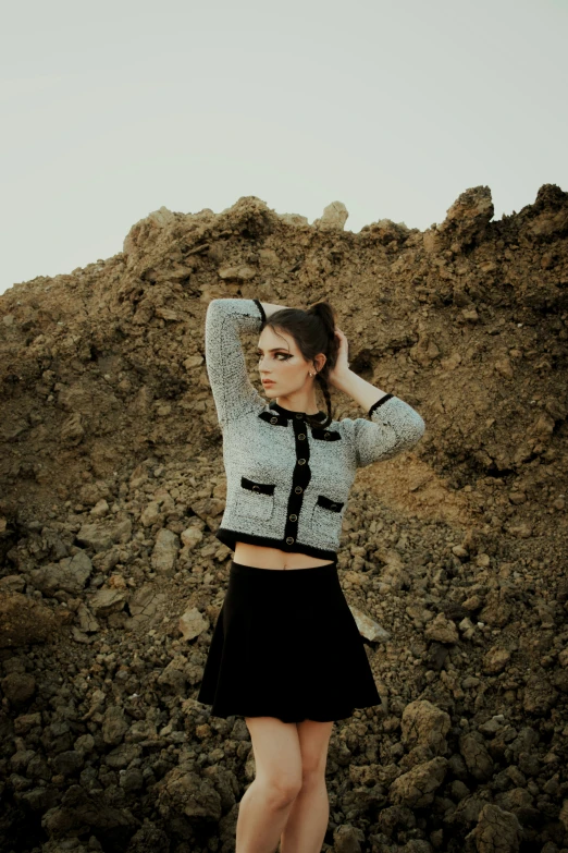 a woman stands in front of a rock mountain with her hands on her hair