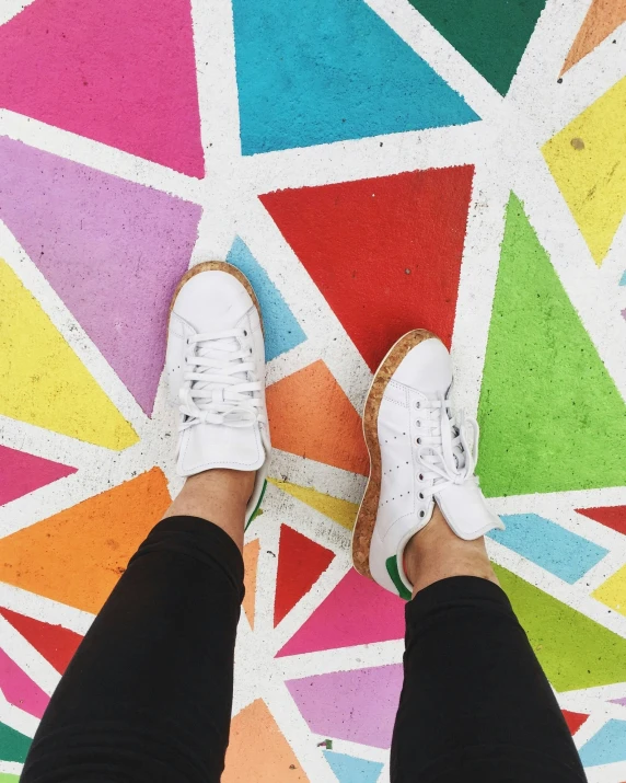 a person wearing white shoes standing on a brightly colored floor