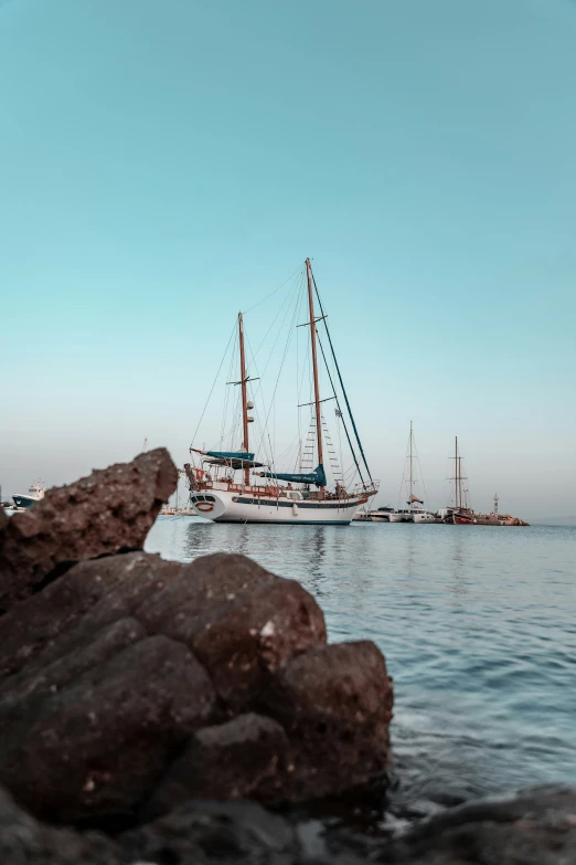 two sail boats moored near rocks on a bay