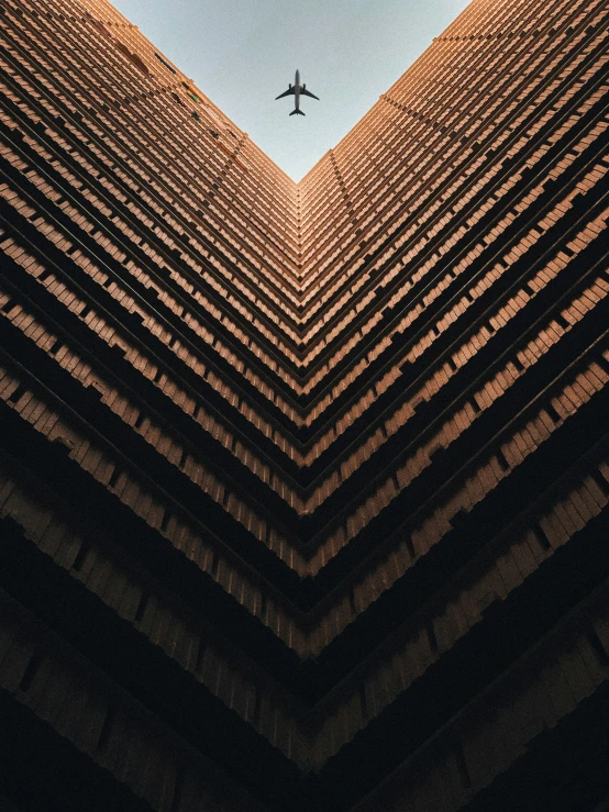 a jet flies through the blue sky over an angled building