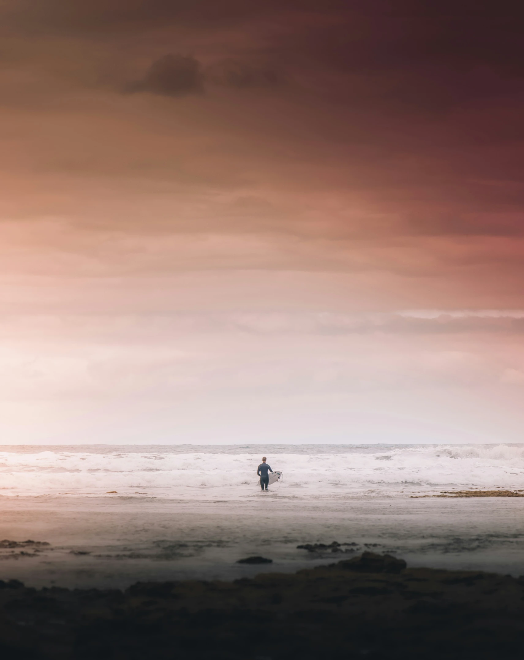 two surfers on the beach under pink clouds