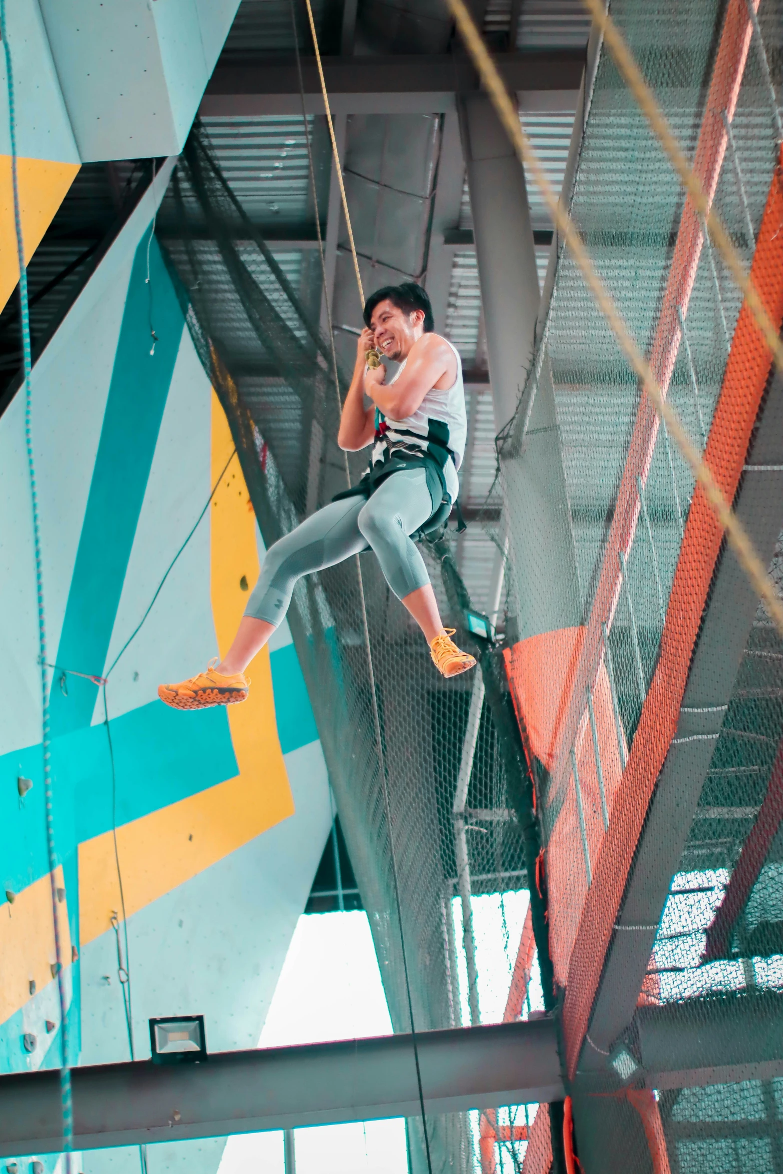 man on ropes above an indoor trampoline doing tricks