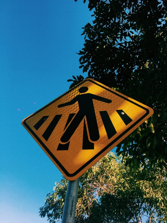 a yellow pedestrian crossing sign on a metal pole