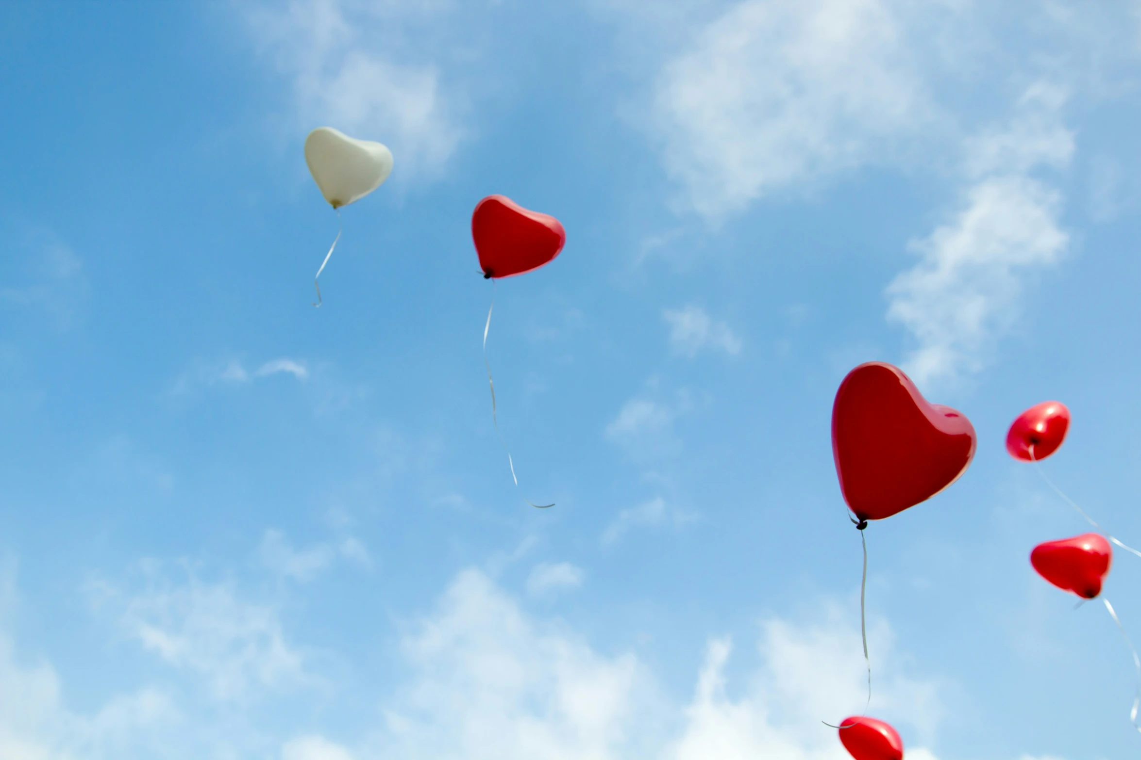 several heart shaped balloons flying in the blue sky