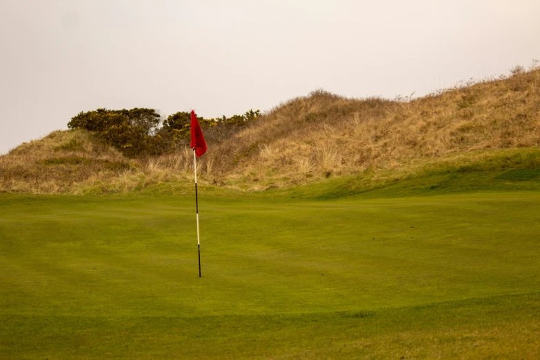 a red flag is in the foreground of a golf course