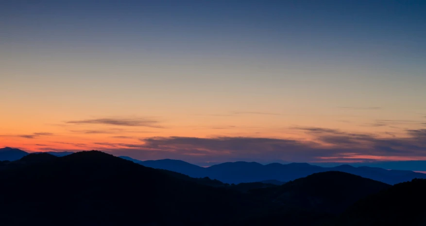 silhouettes of mountains and hills against an orange sky