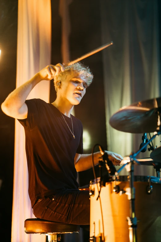 a guy with blonde hair plays drums in a dimly lit room