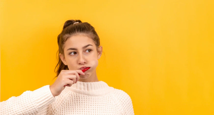 a young woman holding onto her toothbrush with the yellow background behind her