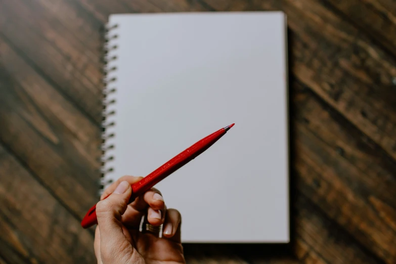 a hand holding a red colored pen while writing on a notebook