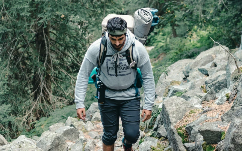 man walking through a rocky trail, looking down on his hat