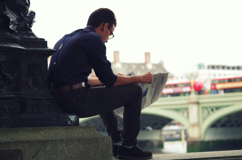 a man is sitting on a stone wall reading a newspaper