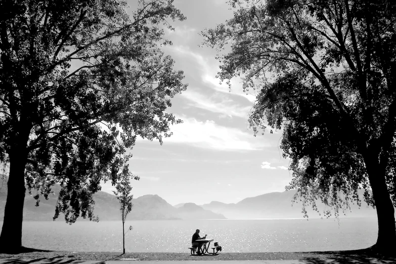 black and white image of a man sitting on his bicycle under trees