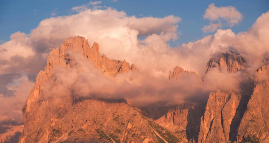 several tall mountains are covered in cloud under blue skies