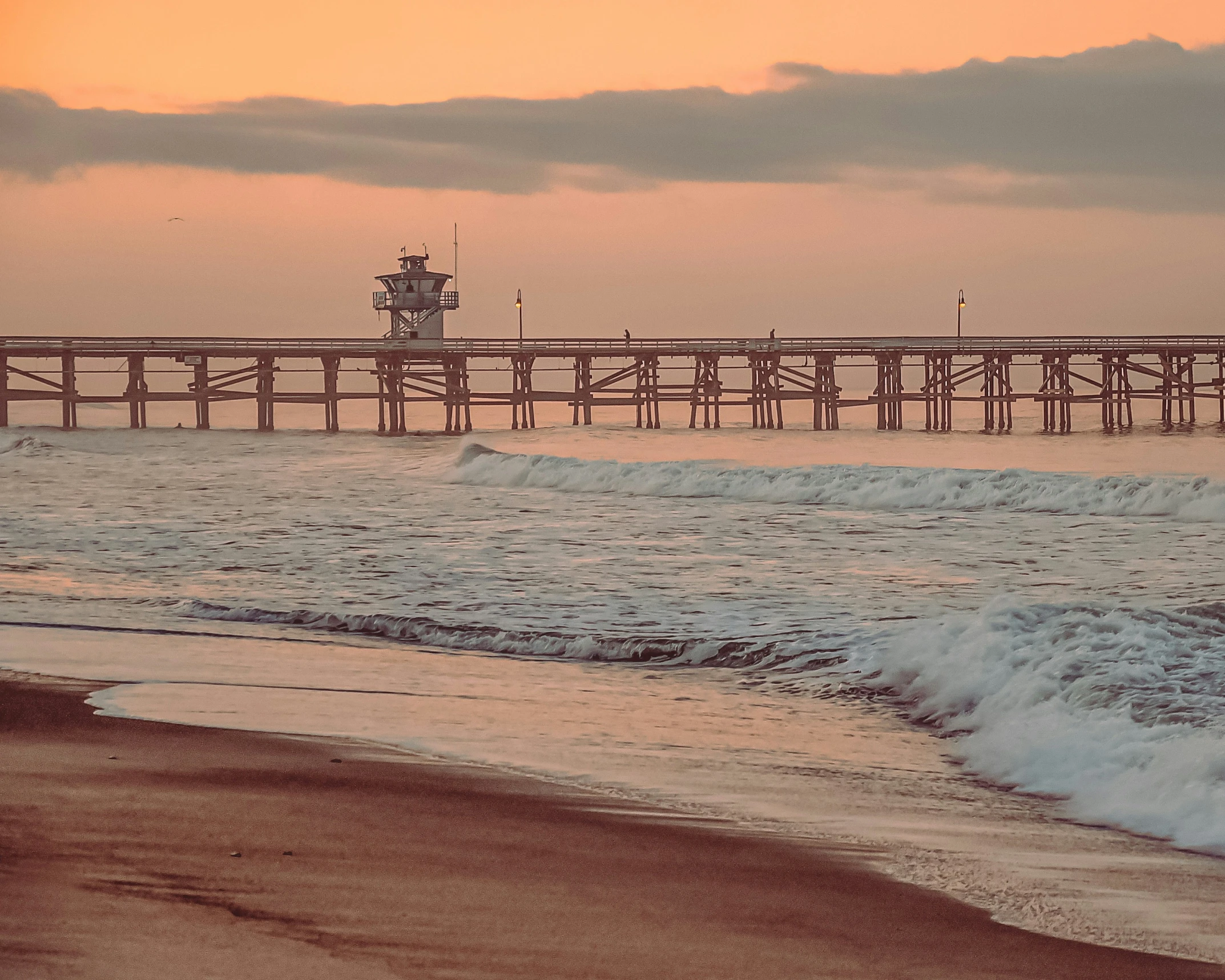 a wooden pier next to a beach at sunset