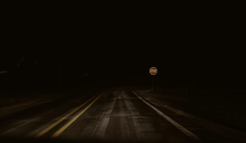 a deserted dark road at night with a stop sign