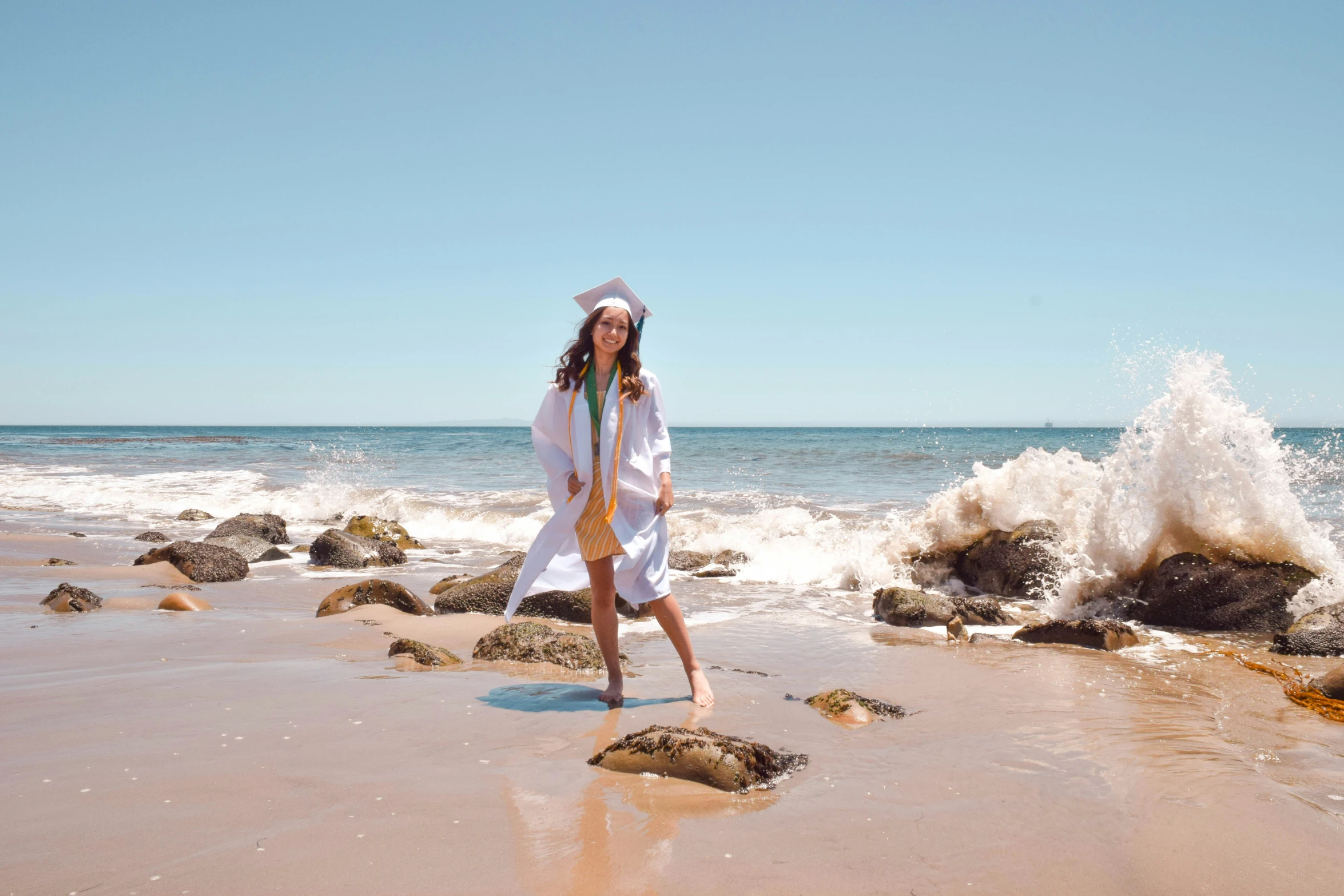 a woman in white standing on rocks next to a body of water