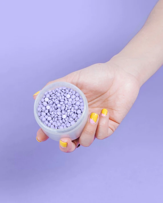 a person is holding a container of purple beads