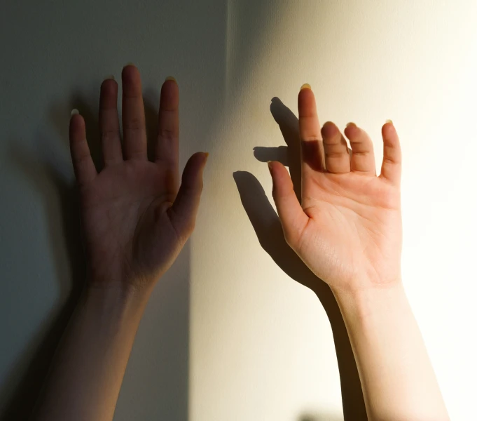 two hands reaching up towards each other next to white wall