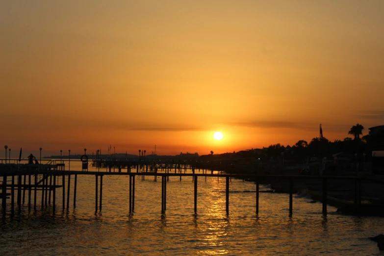 the sun is rising over the water at the end of the pier