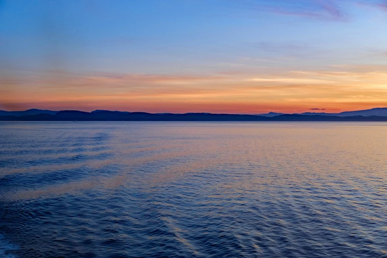 a calm sea as the sun sets behind a hill