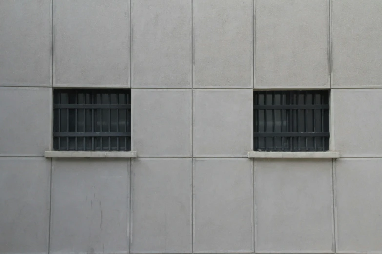 two windows with bars on the sides of them in a large cement wall