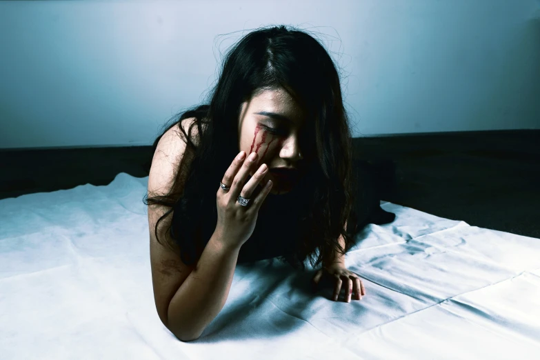 a woman laying on a bed covering her face with one hand