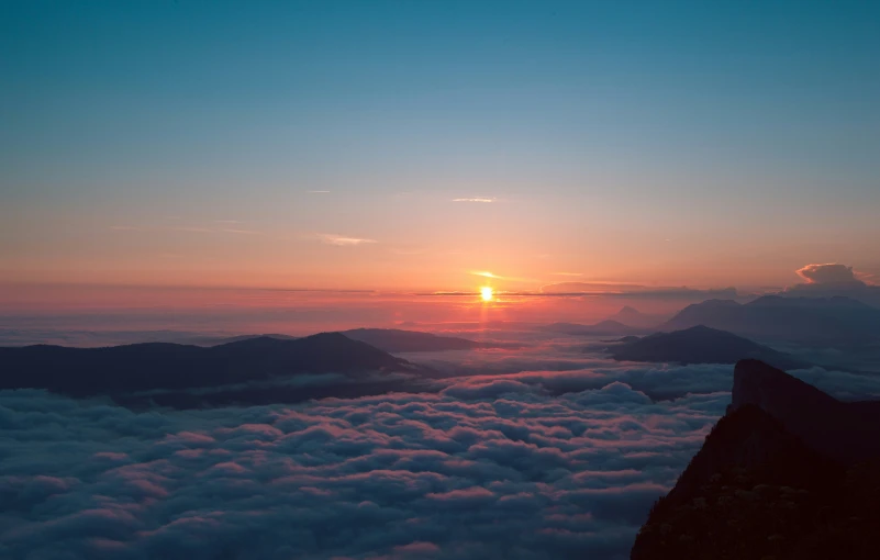 a sunset over some clouds and mountains with the sun shining