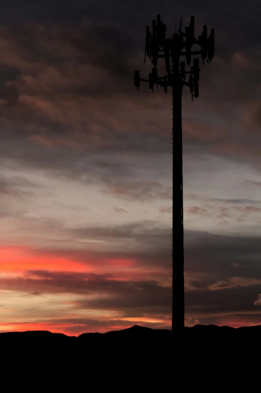 the sun sets behind a tall tower that is silhouetted by clouds