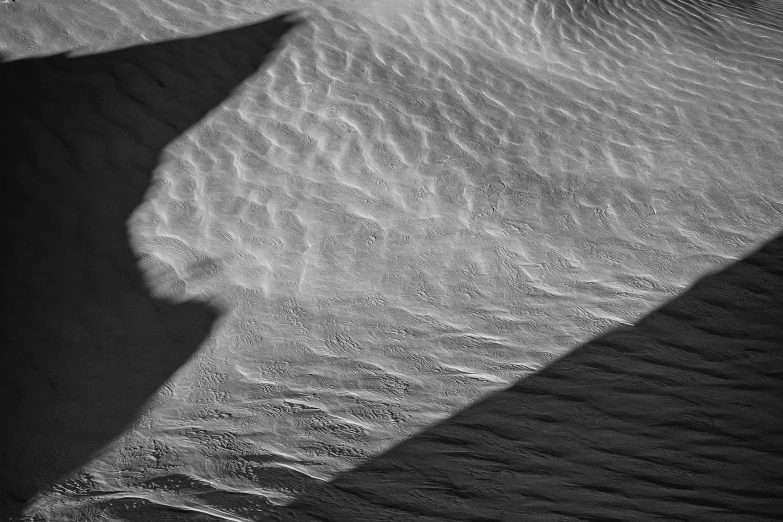 a shadow of a skateboarder riding a rail over sand