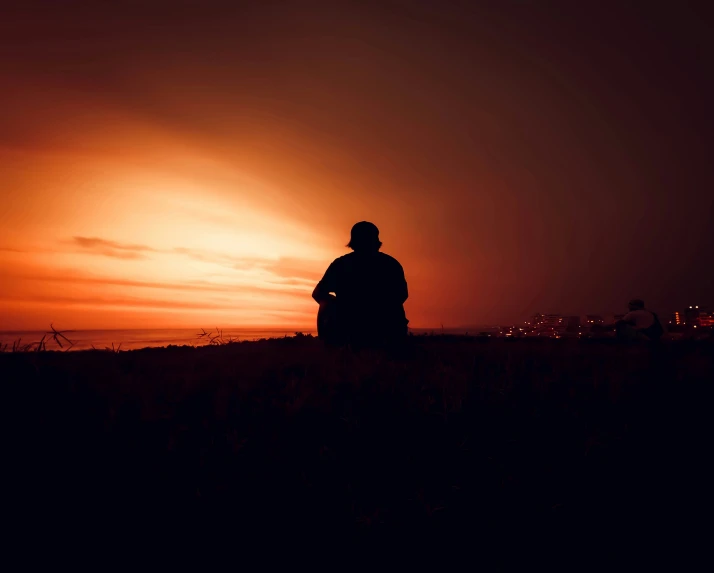 the silhouette of a man sitting against an orange and pink sky