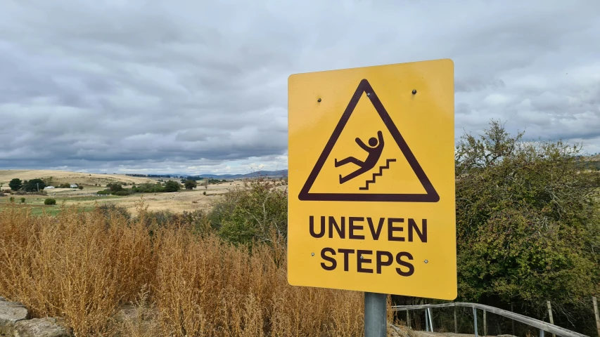 a yellow sign is posted on a pole with dry grass