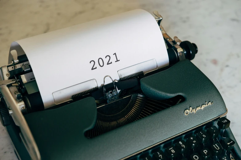 an old fashioned black typewriter with a white sheet reading 2021