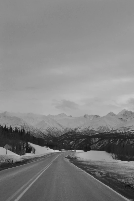 the snow covered road is leading to mountains