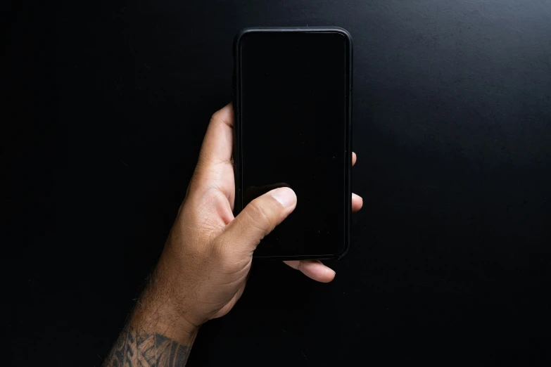 a hand is holding a black phone up against a dark background