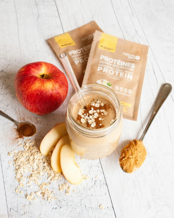 a jar of granola on a white wooden surface with an apple