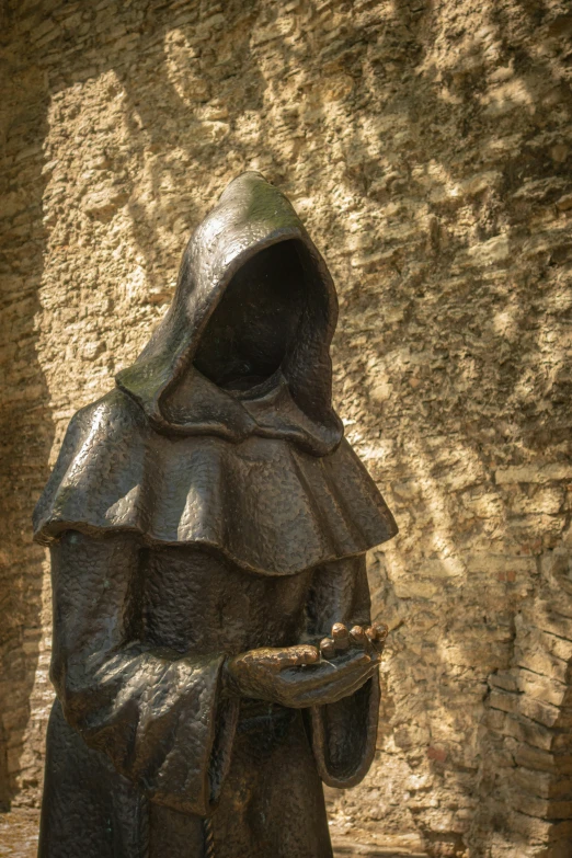 a statue of a hooded woman in front of a brick wall