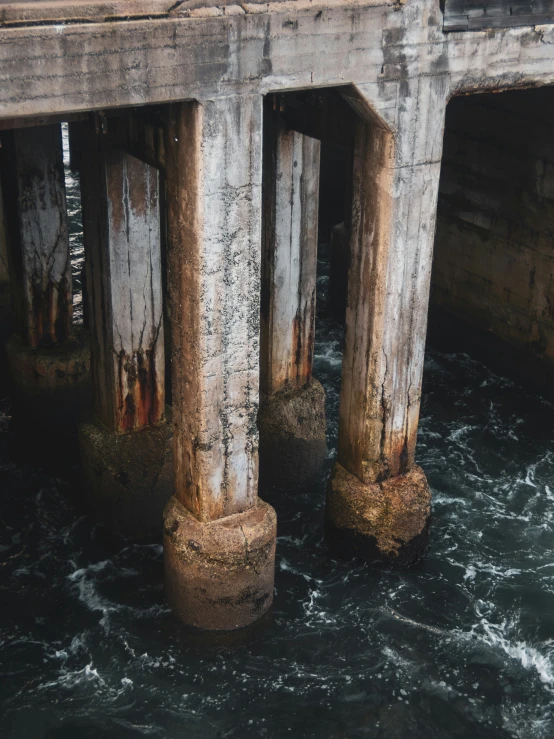 the pillars of an old bridge and the water are foamy