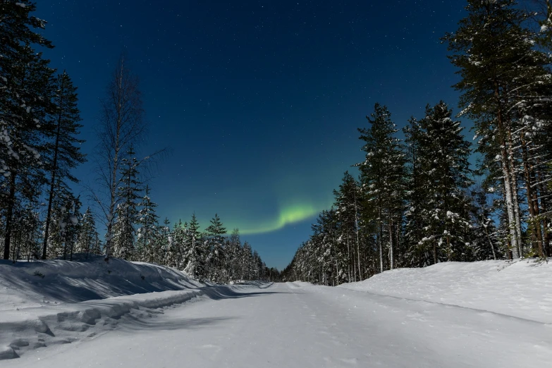 green northern lights and the sky shine above some snowy hills