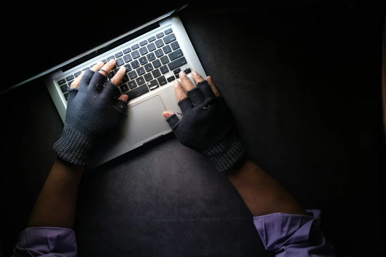 an overhead view of someone wearing gloves while typing on a laptop