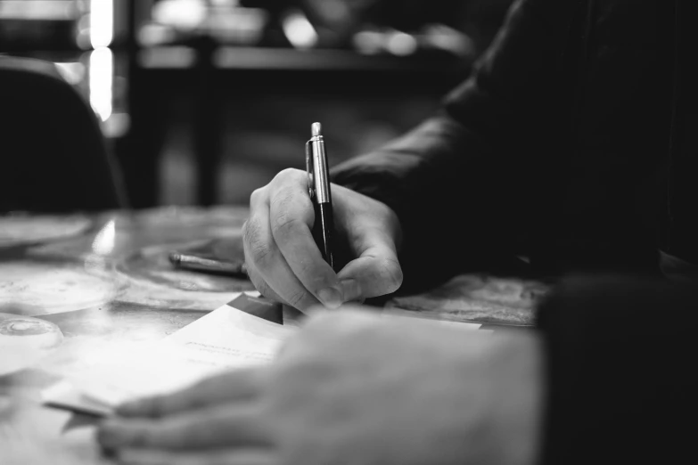 a man is holding a pen over a document at a table