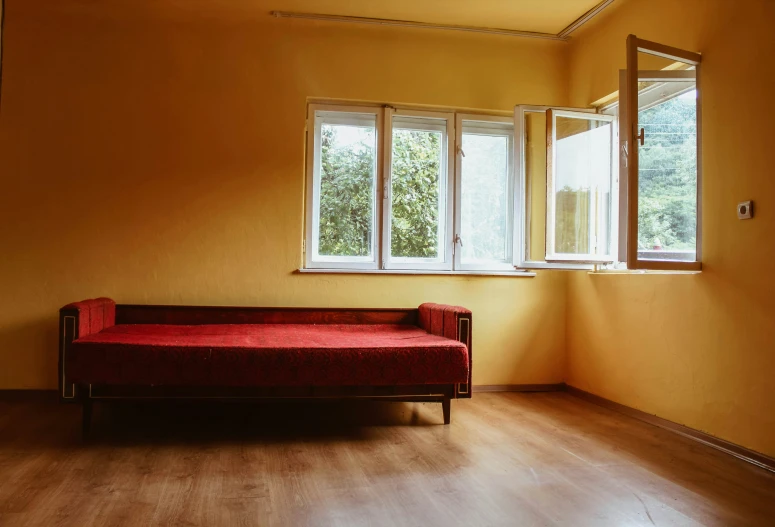 a red couch against a yellow wall with three large windows