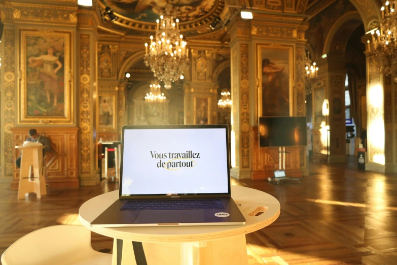 an open laptop computer on a wooden table in front of a chandelier