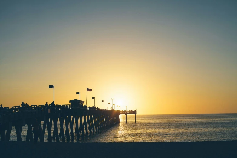 a sunset at the end of a pier next to the ocean