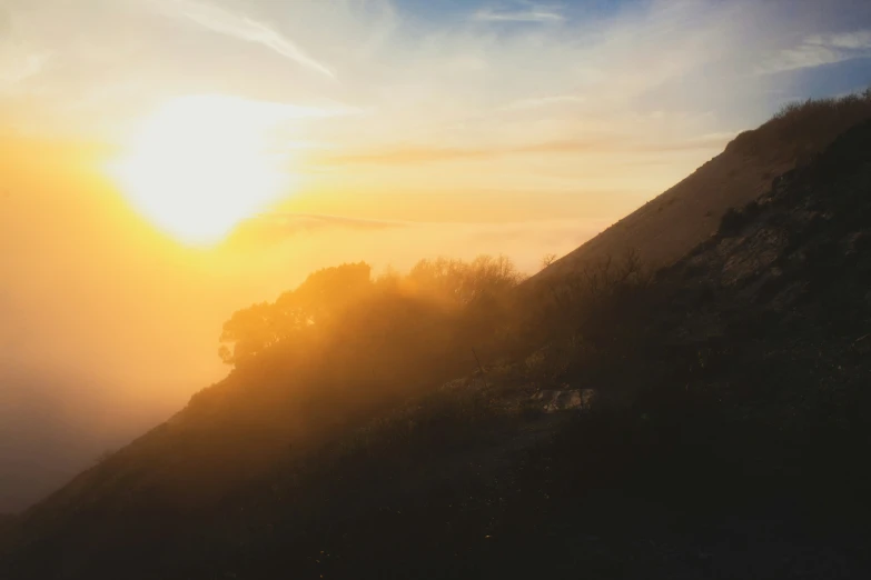 the sun is shining through the fog on the top of a mountain