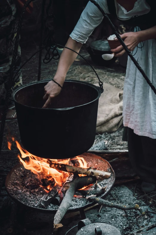 someone stirring soing over an open fire, while wearing a hat