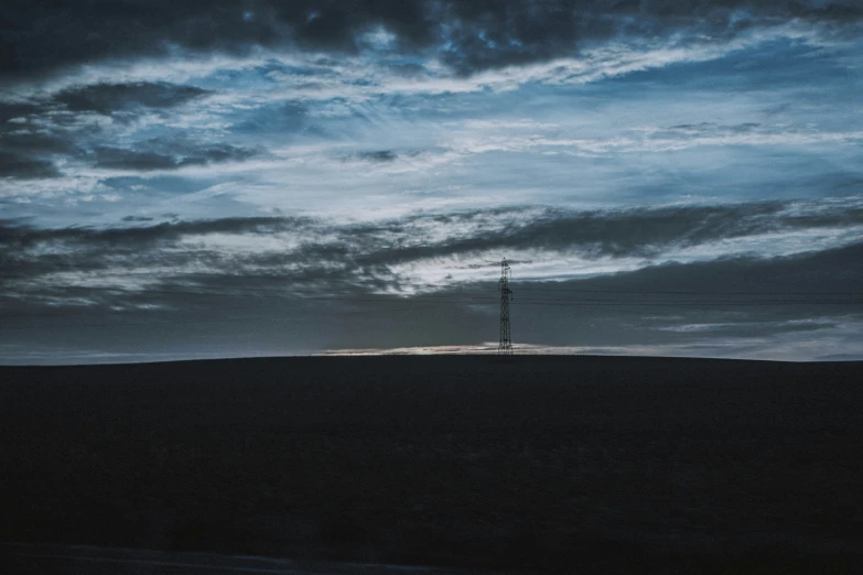 the lone power line stands in the distance as clouds roll by