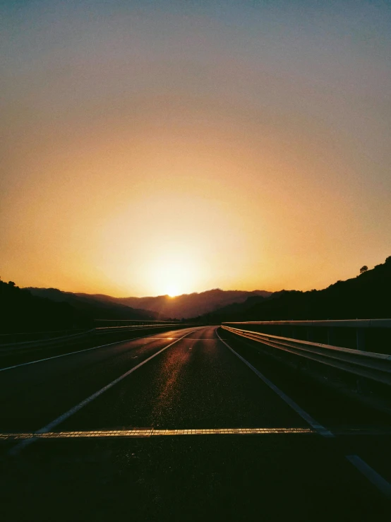 the sun is setting behind mountains and highway lines