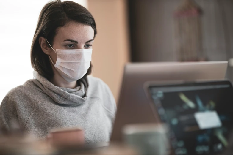 woman with white face mask typing on a laptop computer