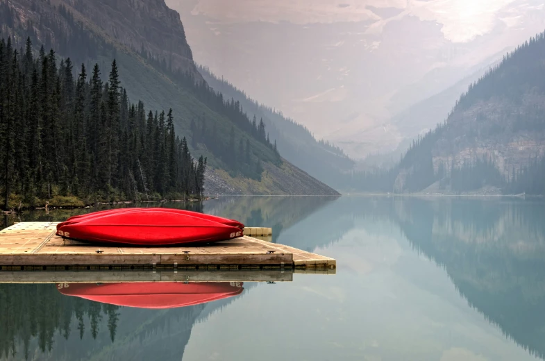 a red boat laying in water near some pine trees