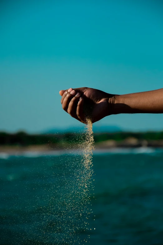 a hand holding sand on the beach in the day